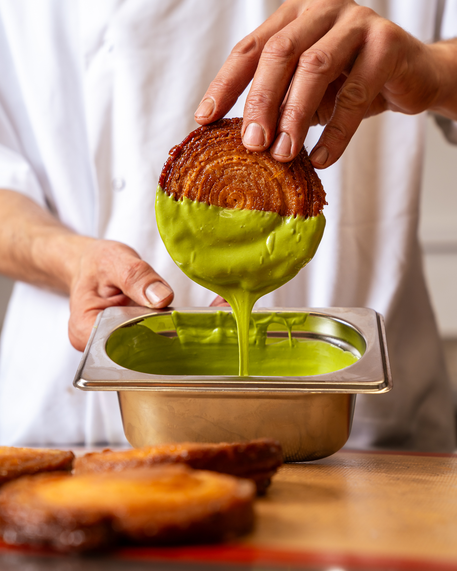 Chef dipping a fresh pastry into pistachio glaze